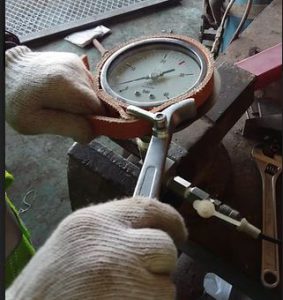Removing the glass cover of a pressure gauge using a strap wrench.